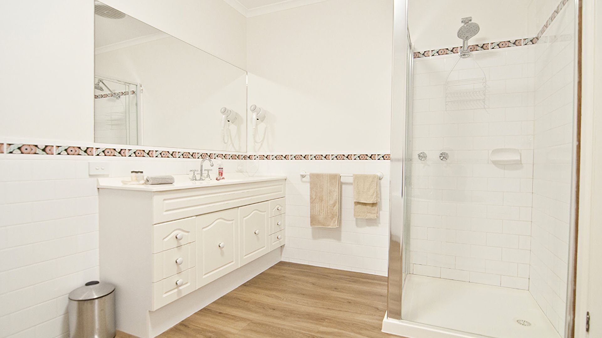 Un baño con tocador blanco, ducha y salpicadero de azulejos.