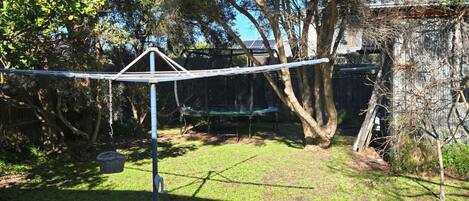 A backyard with a trampoline, a swing set, and a tree.