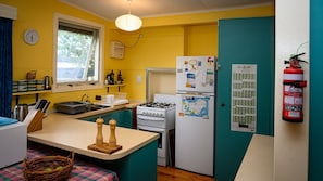 A compact kitchen with a gas stove, a refrigerator, a sink, and a window with curtains.