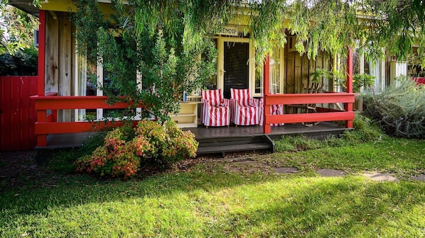 A house with a red porch, a yellow door, and a small garden area with red and white striped chairs.