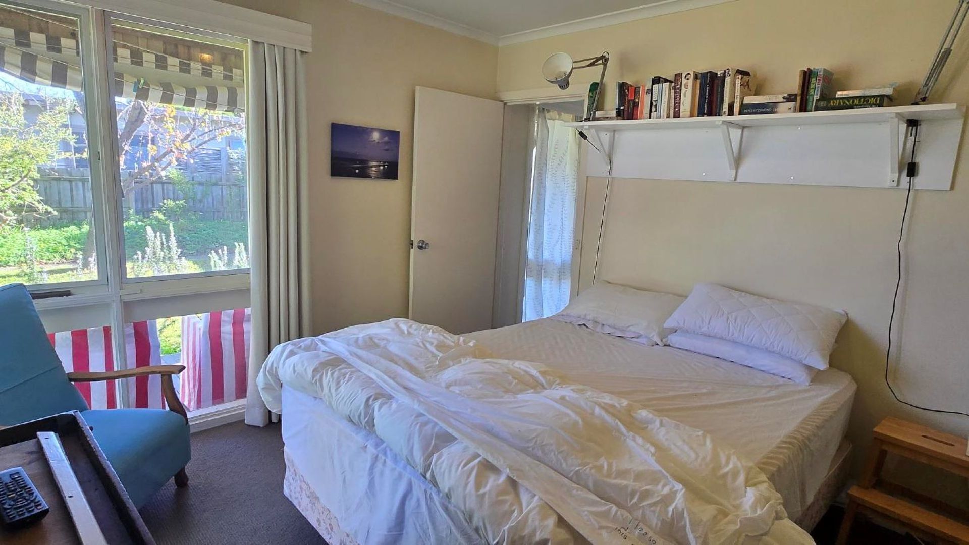 A bedroom with a bed, a chair, a desk, a window with curtains, and a bookshelf with books.