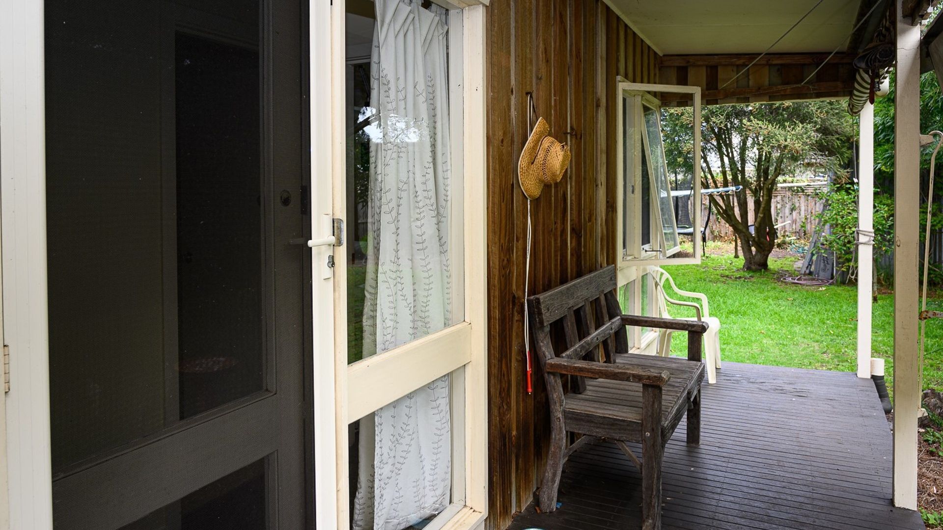 A wooden porch with a bench, a hanging light fixture, and a view of a grassy yard.