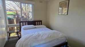 Quarto com cama, uma cadeira, janela e um quadro na parede.