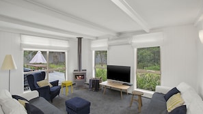 A modern living room with a fireplace, comfortable seating, a flat-screen TV, and large windows offering a view of greenery.