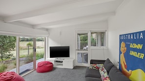 A modern living room with a flat-screen TV, a red bean bag, a grey sofa, and a colorful poster on the wall.