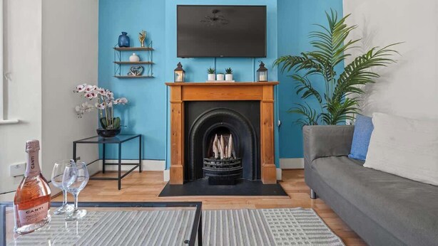 Ein Wohnzimmer mit blauer Wand, Kamin, einer Couch und einem Fernseher, der über dem Kamin angebracht ist.
