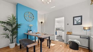 Ein modernes Wohnzimmer mit blauer Akzentwand, einer runden Uhr, einem Esstisch mit Stühlen, einer großen Kübelpflanze und einer kleinen Bank.