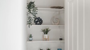 Ein weißes Regal mit verschiedenen Dekorationselementen, darunter Pflanzen, eine Muschel und eine Holzskulptur.
