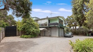 Une maison à deux étages avec un garage, une voiture garée dans l’allée et un grand arbre devant.
