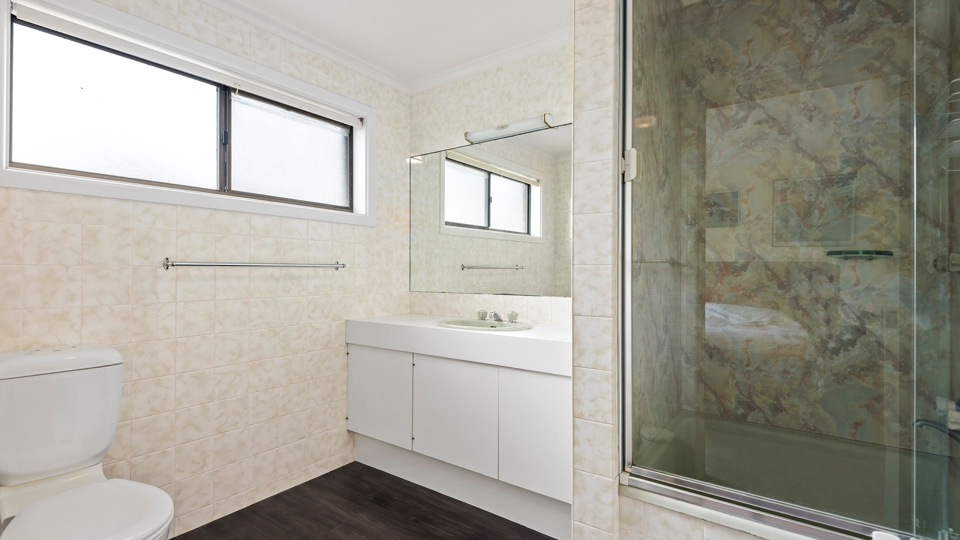 A bathroom with a toilet, sink, mirror, and shower area.