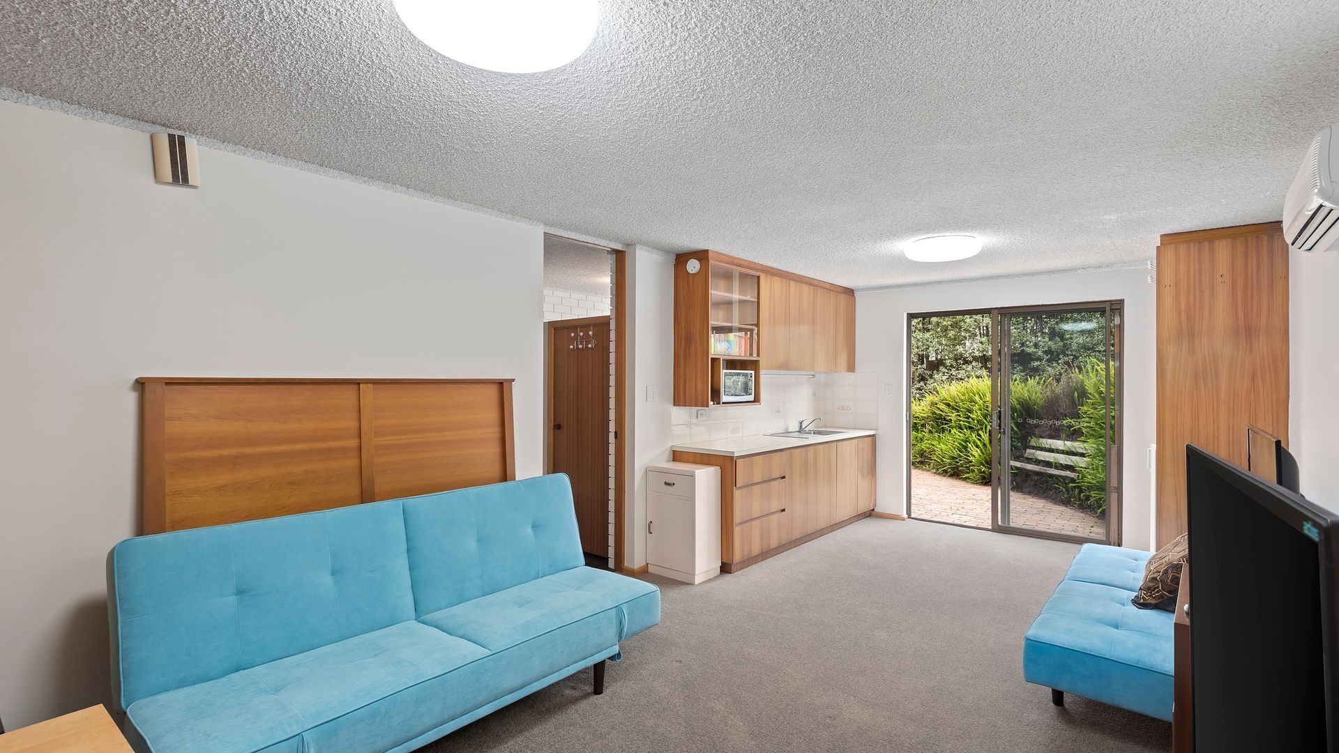 Un espacio habitable moderno y funcional con sofá, kitchenette y puerta corrediza de vidrio que da a un jardín.