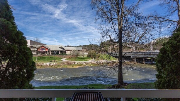 A river with a bridge in the background, a building with a red roof, and a bench in the foreground. - Riverfront Condo Pigeon Forge/Mt. LeConte Views (Pigeon Forge)