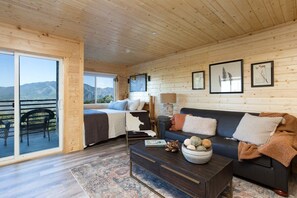 Ein Zimmer mit einem Bett, einer Couch, einem Couchtisch und Blick auf Berge durch eine Schiebetür.