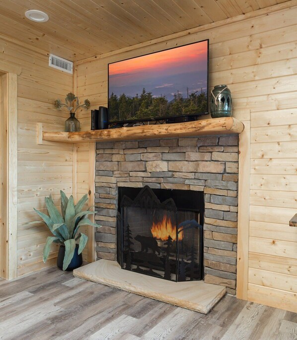 A wooden interior with a stone fireplace, a mounted television, and a potted plant.