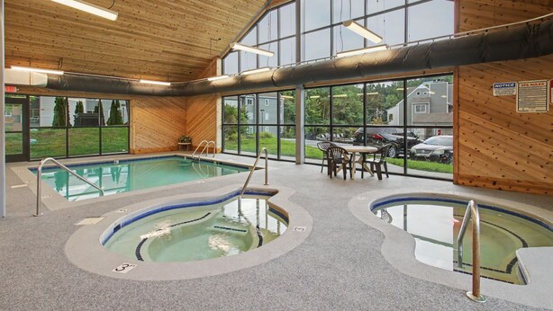 Un espace piscine intérieure comprenant plusieurs bassins, un coin salon et de grandes fenêtres.