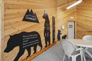 Een kamer met houten wanden, een tafel, stoelen en een muur met bergsilhouetten en tekst.