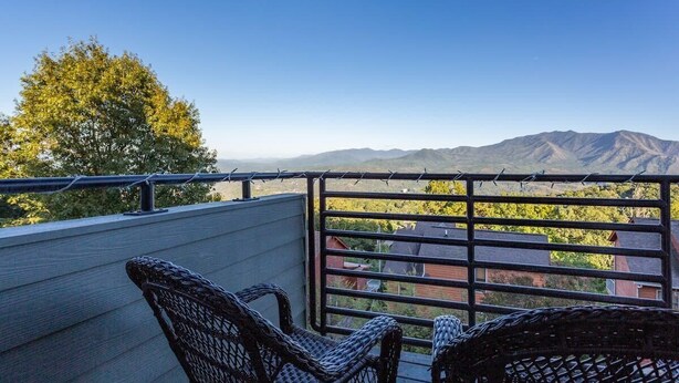 A balcony with wicker chairs, a metal railing, and a view of distant mountains. - Outstanding Mt. LeConte View/Indoor Pool & Hot Tub (Gatlinburg)