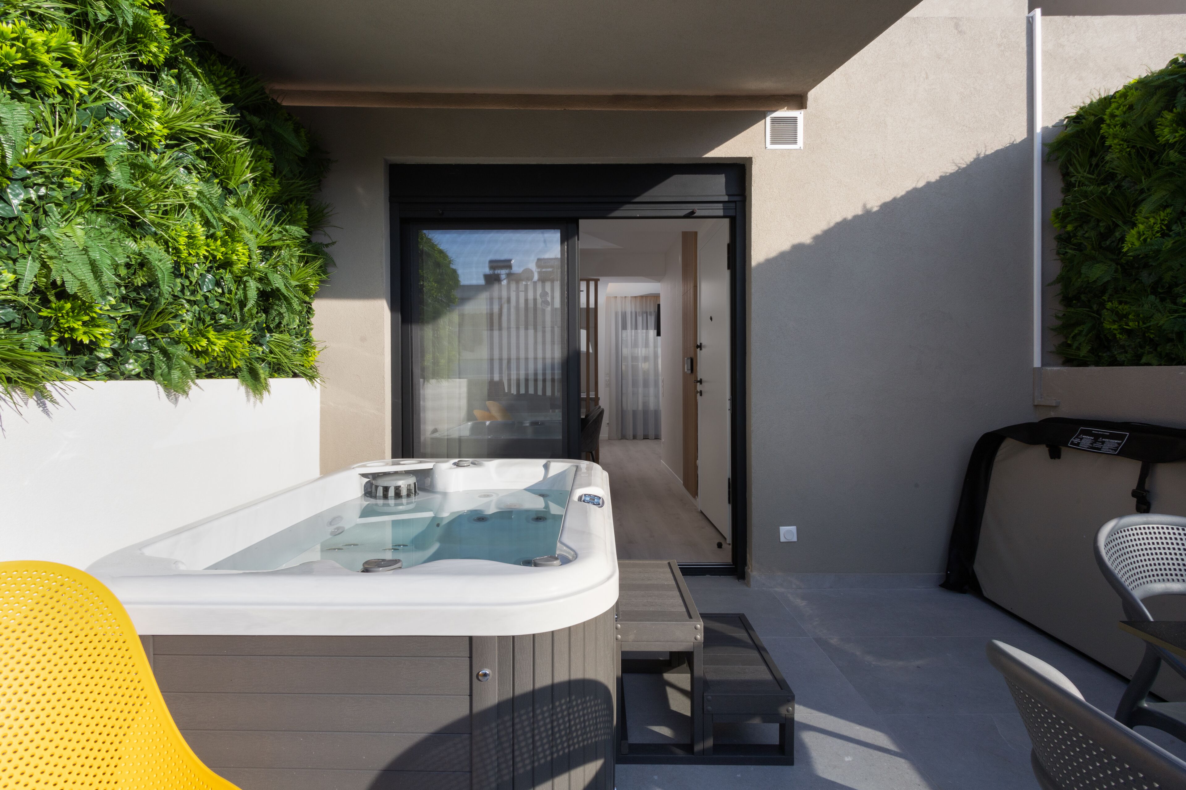 Un espace moderne aménagé à l’extérieur avec un jacuzzi, une paroi en verre, un banc en bois et une chaise.