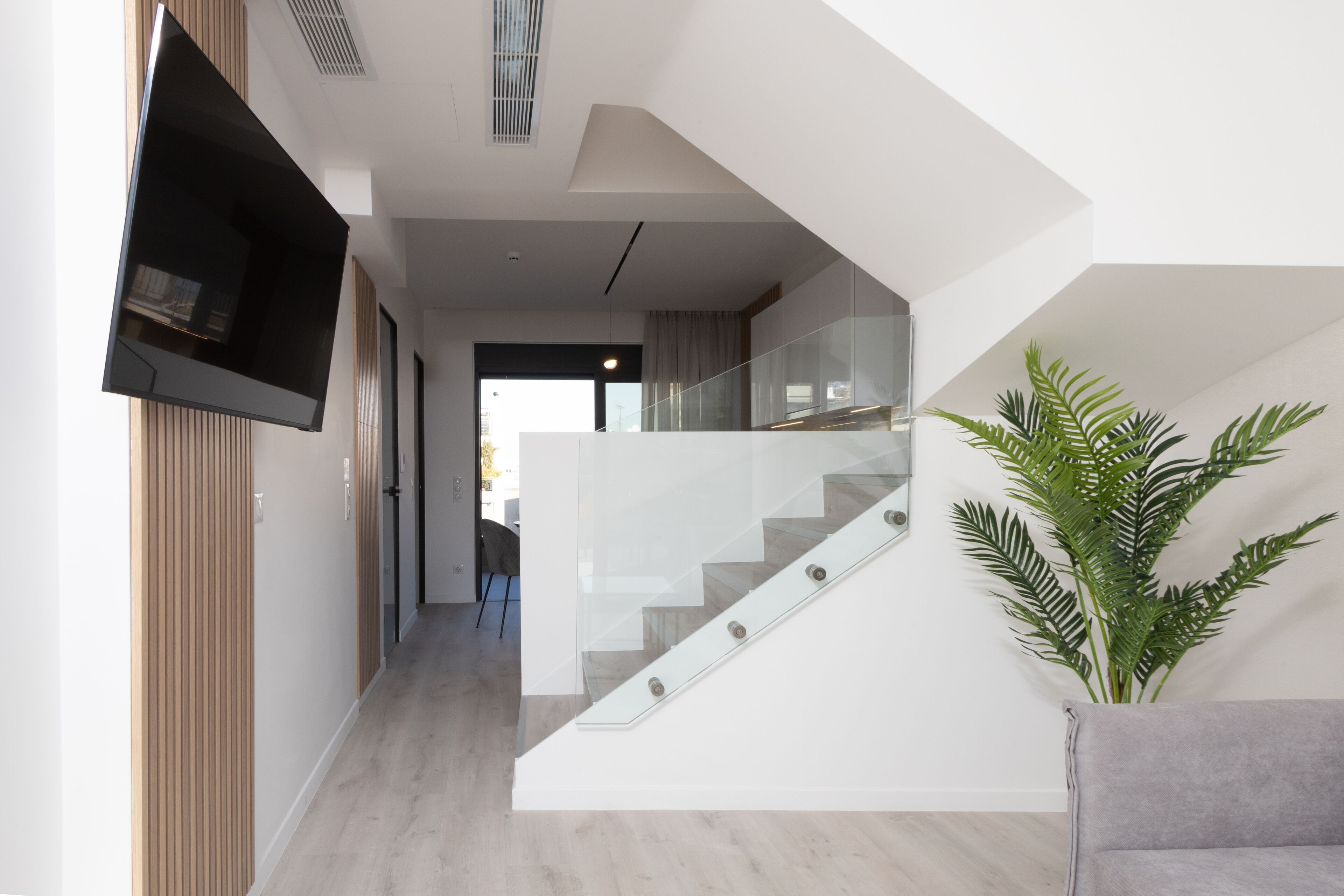 A modern interior with a staircase, a flat-screen TV mounted on a wall, and a potted plant.