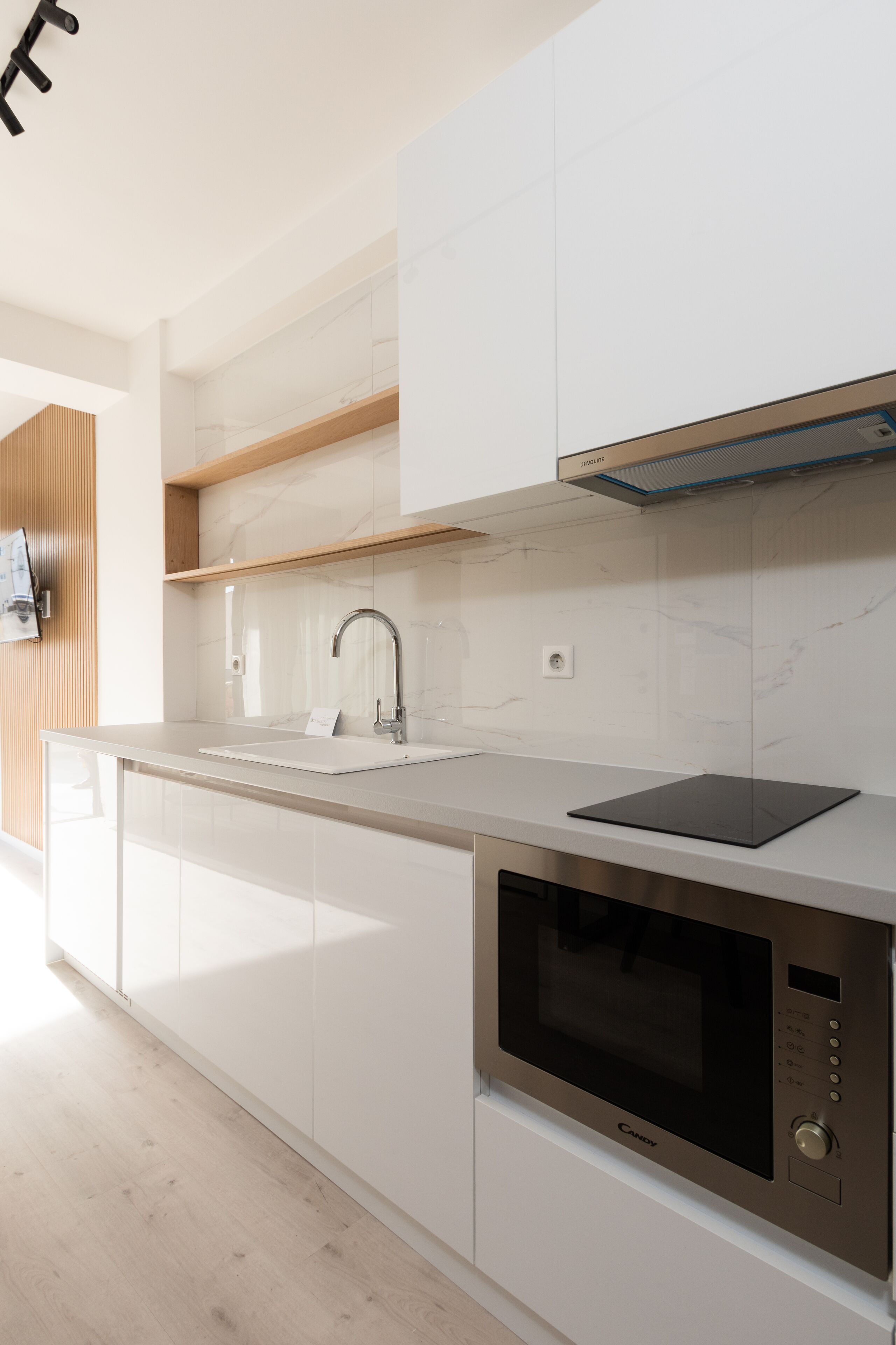 Una cucina moderna con forno a microonde integrato, lavello in acciaio inossidabile e scaffali in legno.