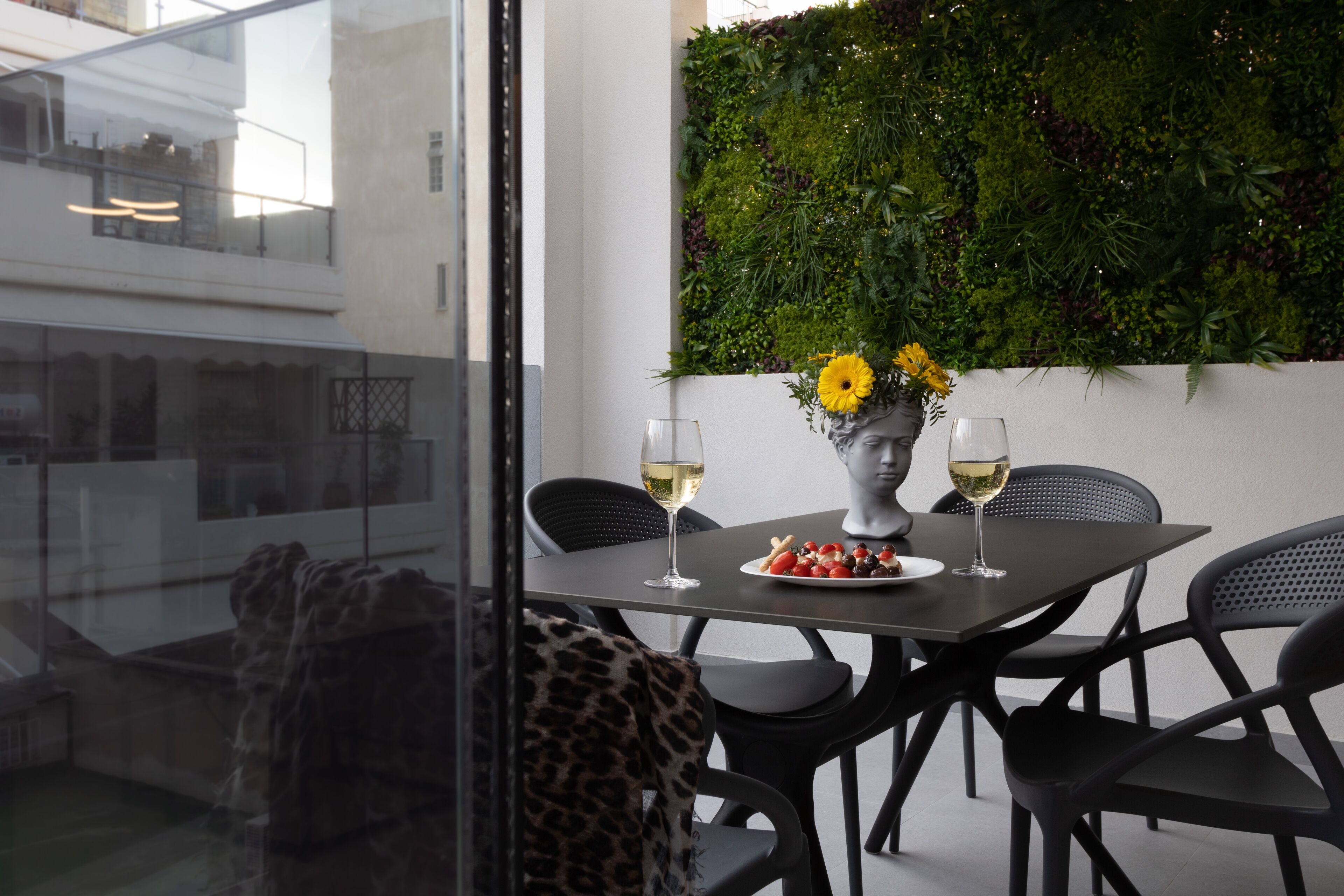 A dining area with a table set for two, featuring a vase with yellow flowers and a plate of food.
