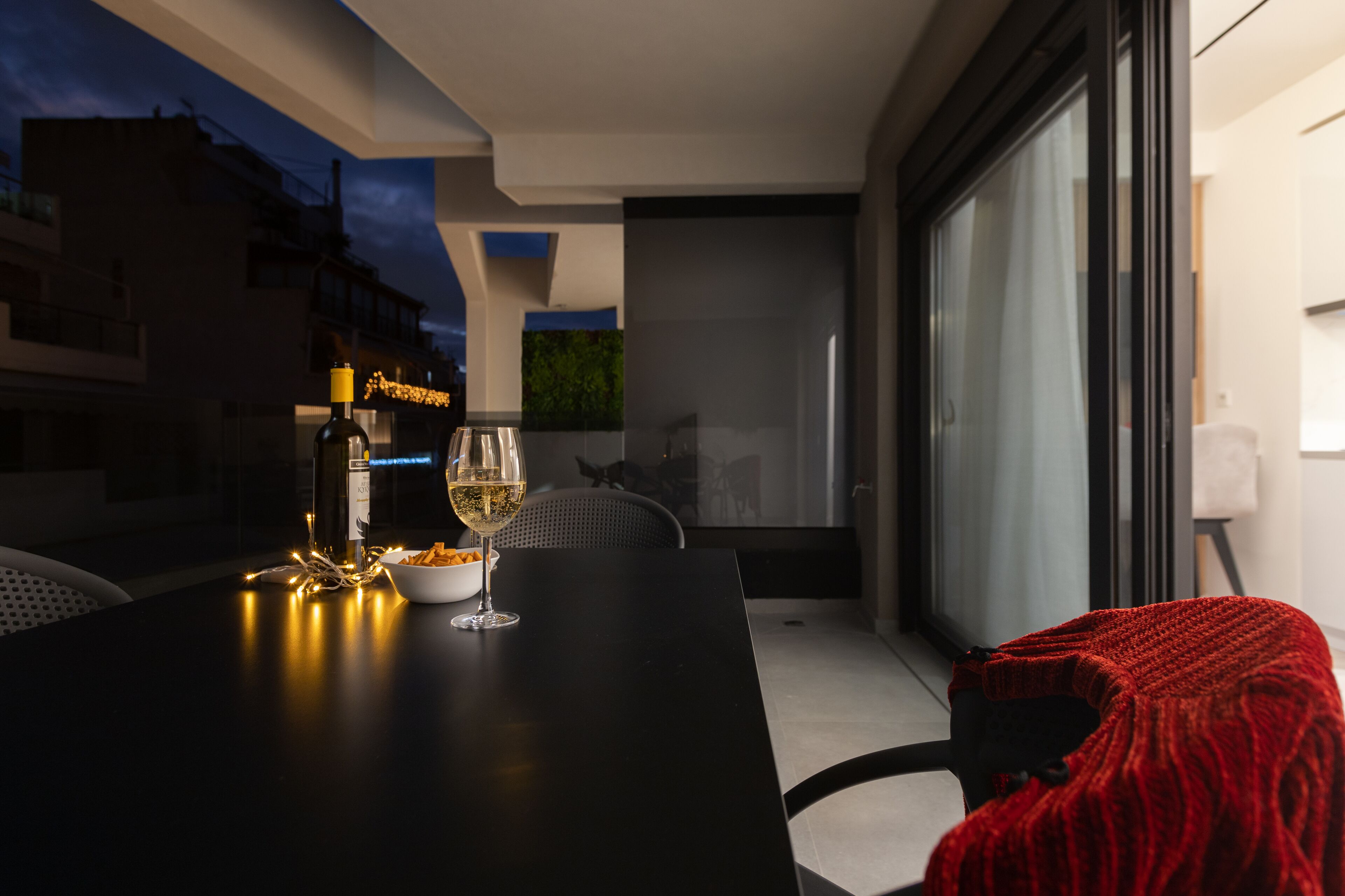 A modern dining area with a table set for two, featuring a bowl of snacks and a glass of white wine.