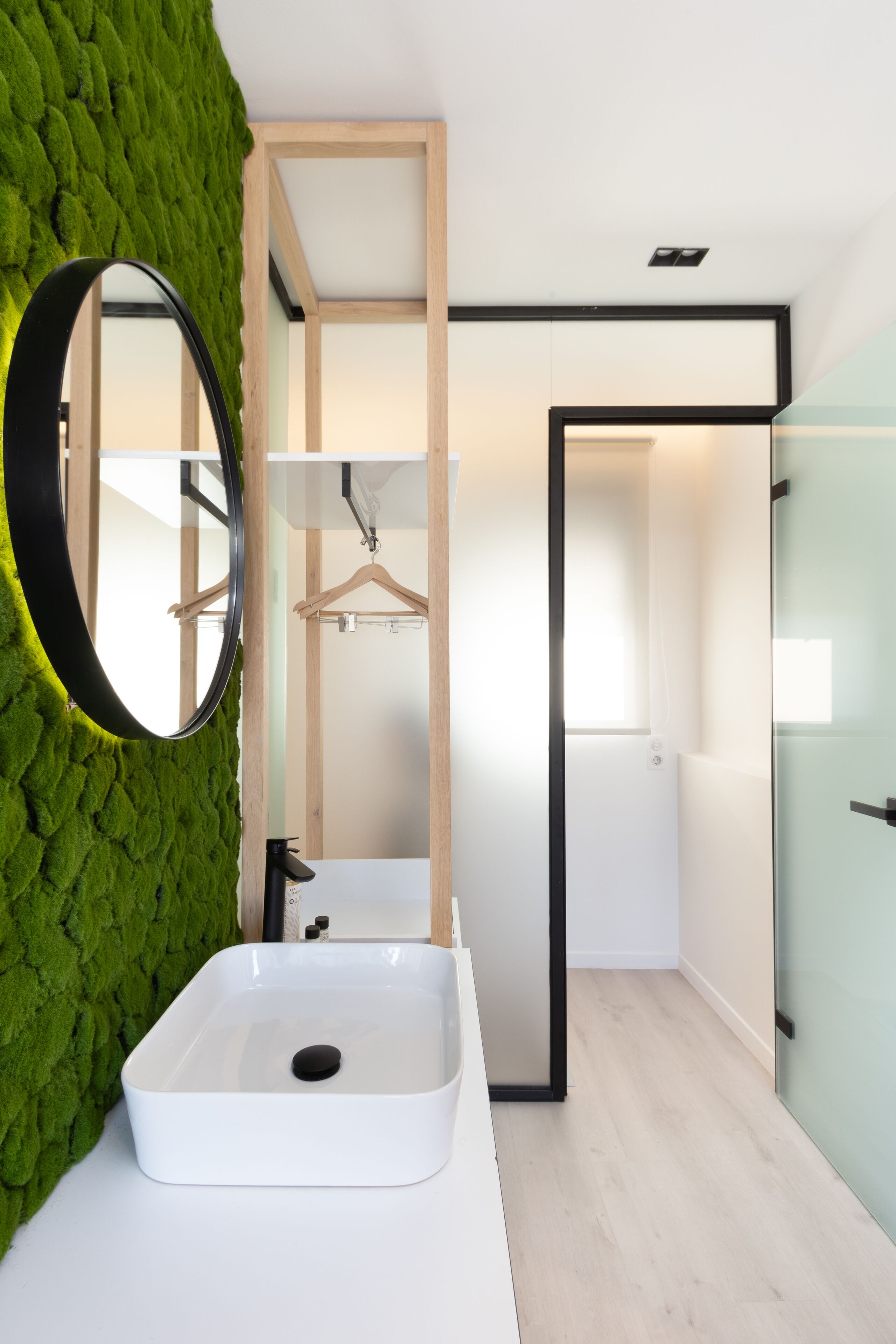 Ein modernes Badezimmer mit einem weißen Waschbecken, einem Spiegel und einer grünen Wand mit Moos.