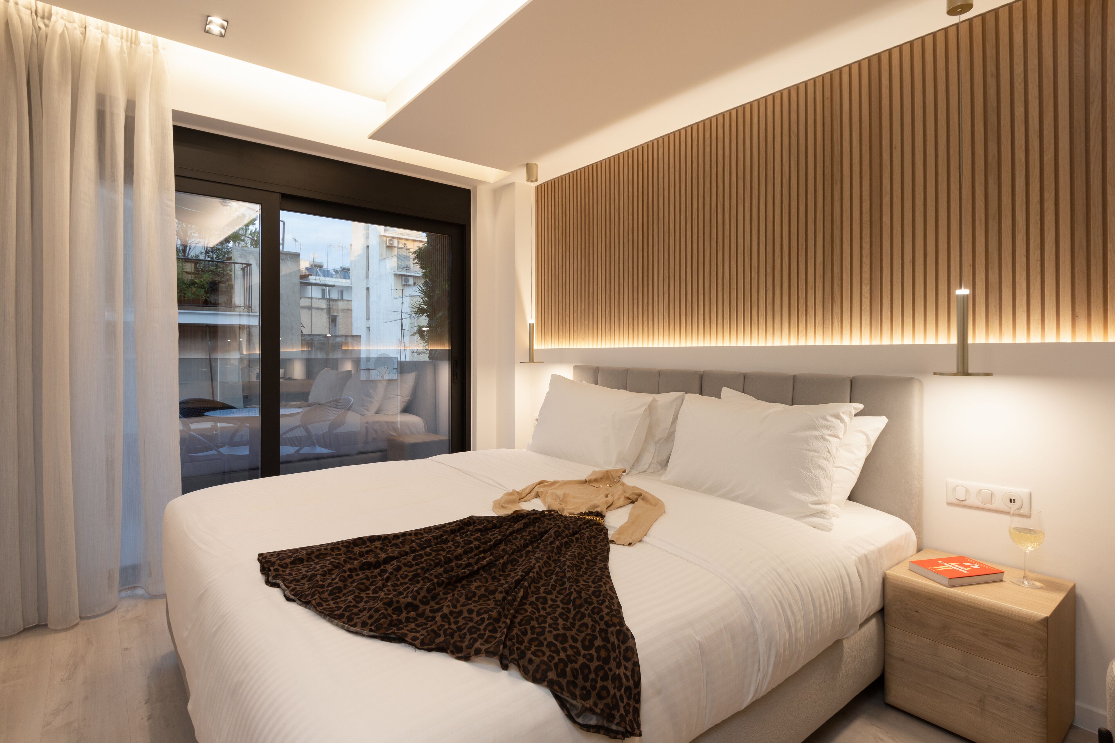 A modern hotel room with a large bed, a nightstand, a lamp, and a view of the outside balcony.