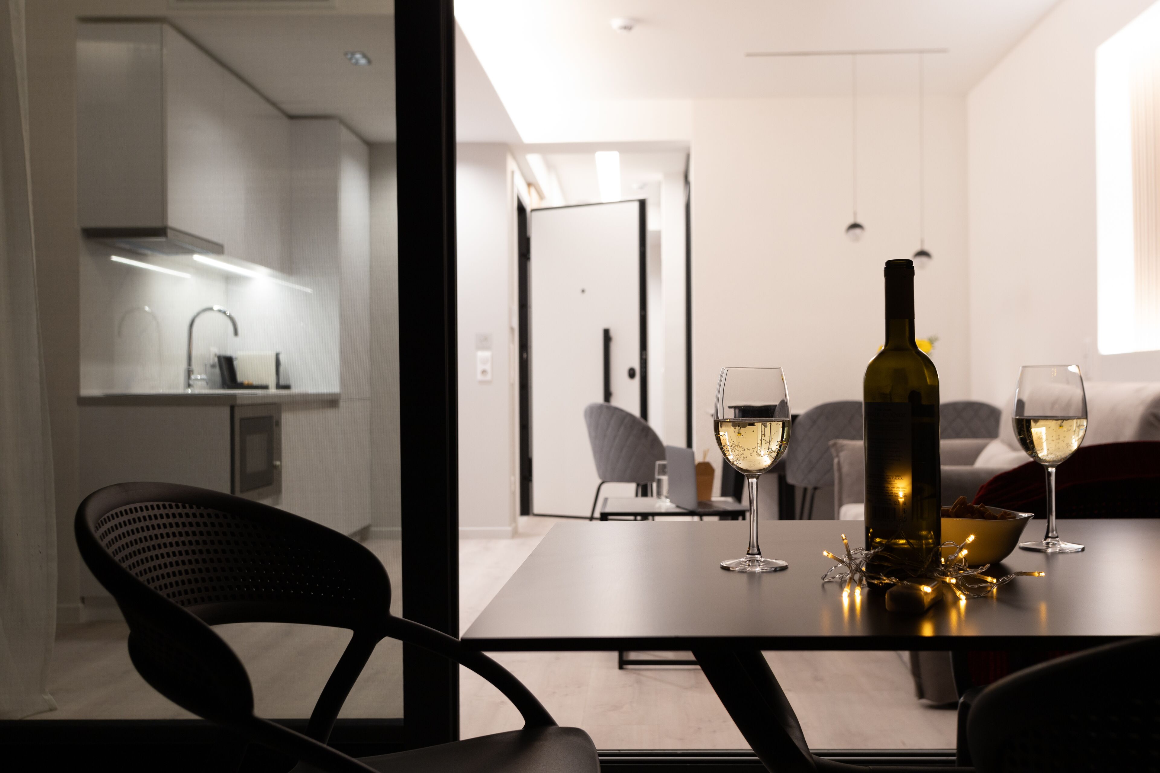 A modern dining area with a table set for two, featuring a bottle of wine and glasses.