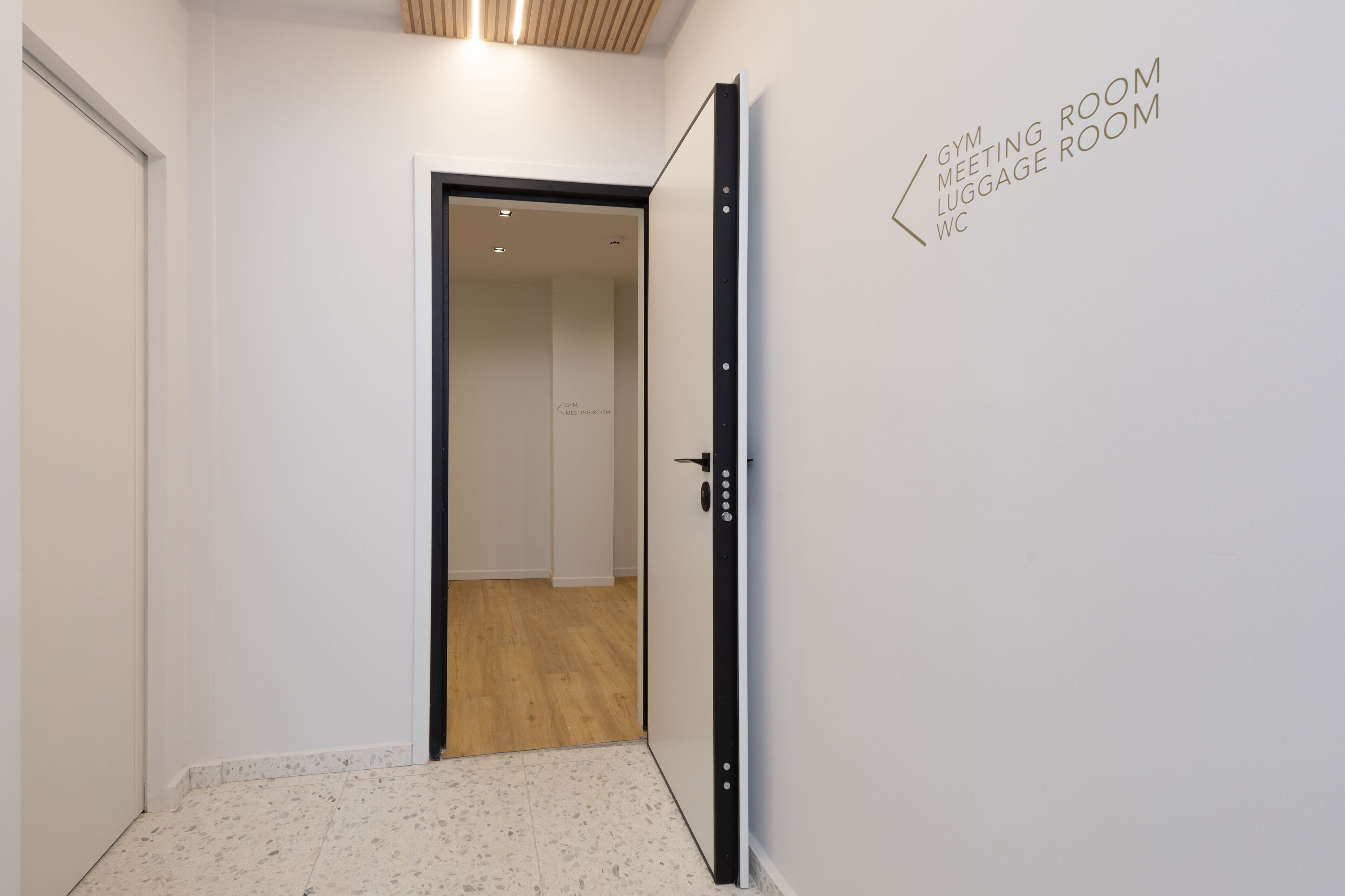 A hallway leading to a gym meeting room with a wooden floor and a white door.