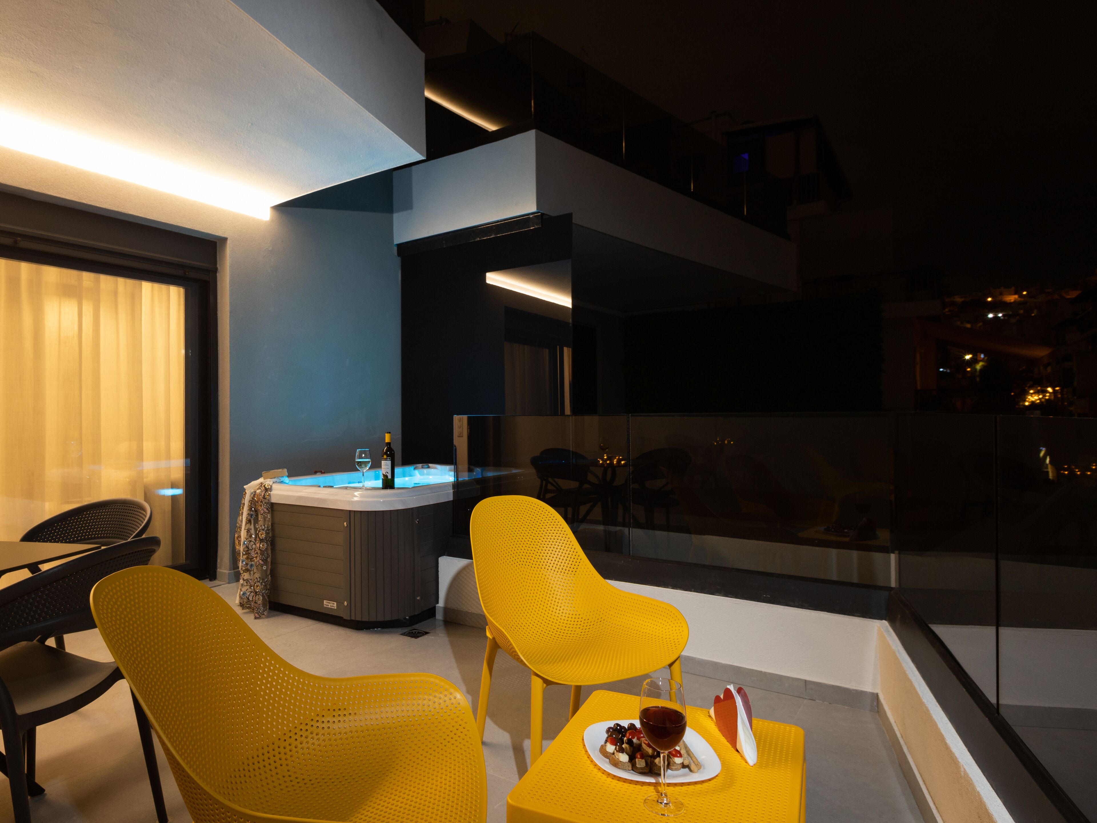 Un espace extérieur moderne, aménagé avec des chaises jaunes, un jacuzzi et une balustrade en verre offrant une vue sur le paysage urbain.