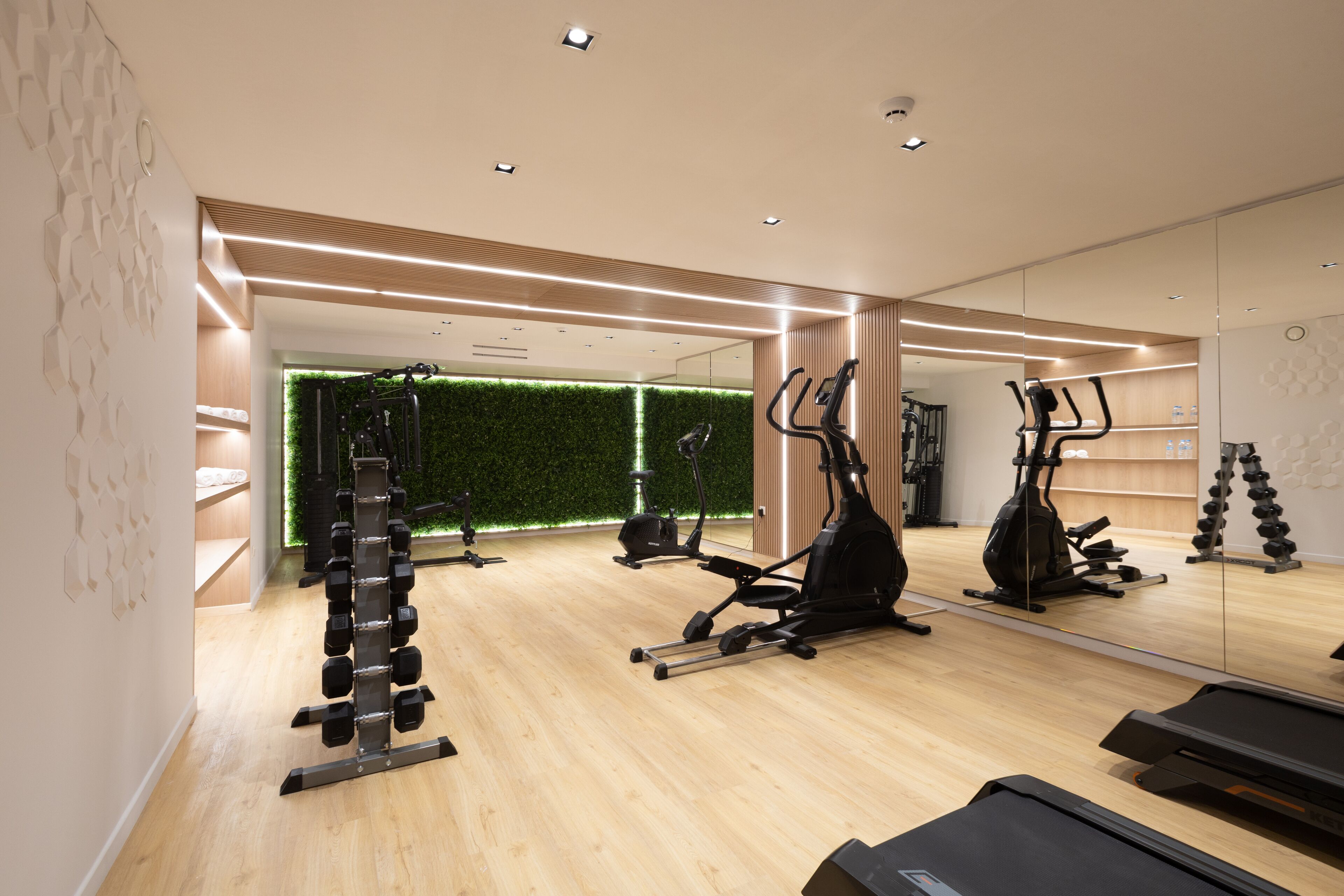 Un gimnasio moderno con equipo de ejercicio, una pared verde y suelo de madera.