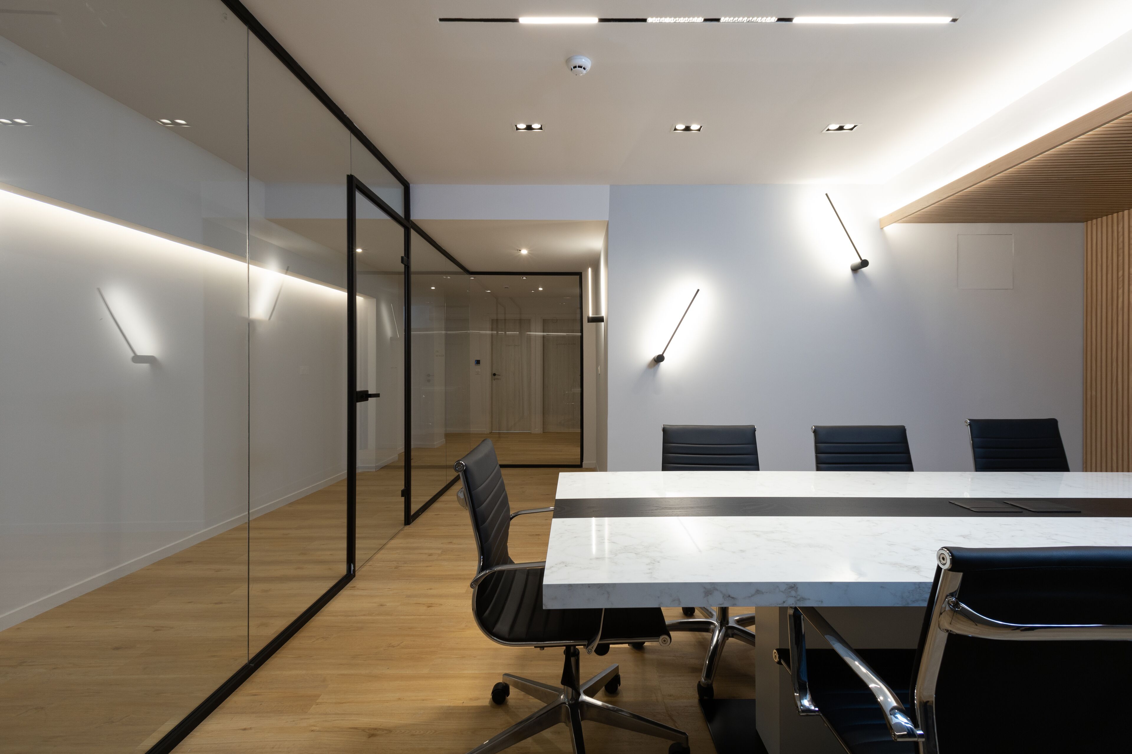 Una sala conferenze moderna con parete divisoria in vetro, un tavolo lungo e quattro sedie.