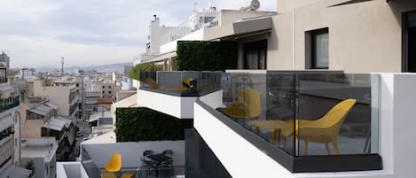 A modern building with a rooftop terrace featuring a hot tub, yellow chairs, and a glass balustrade.