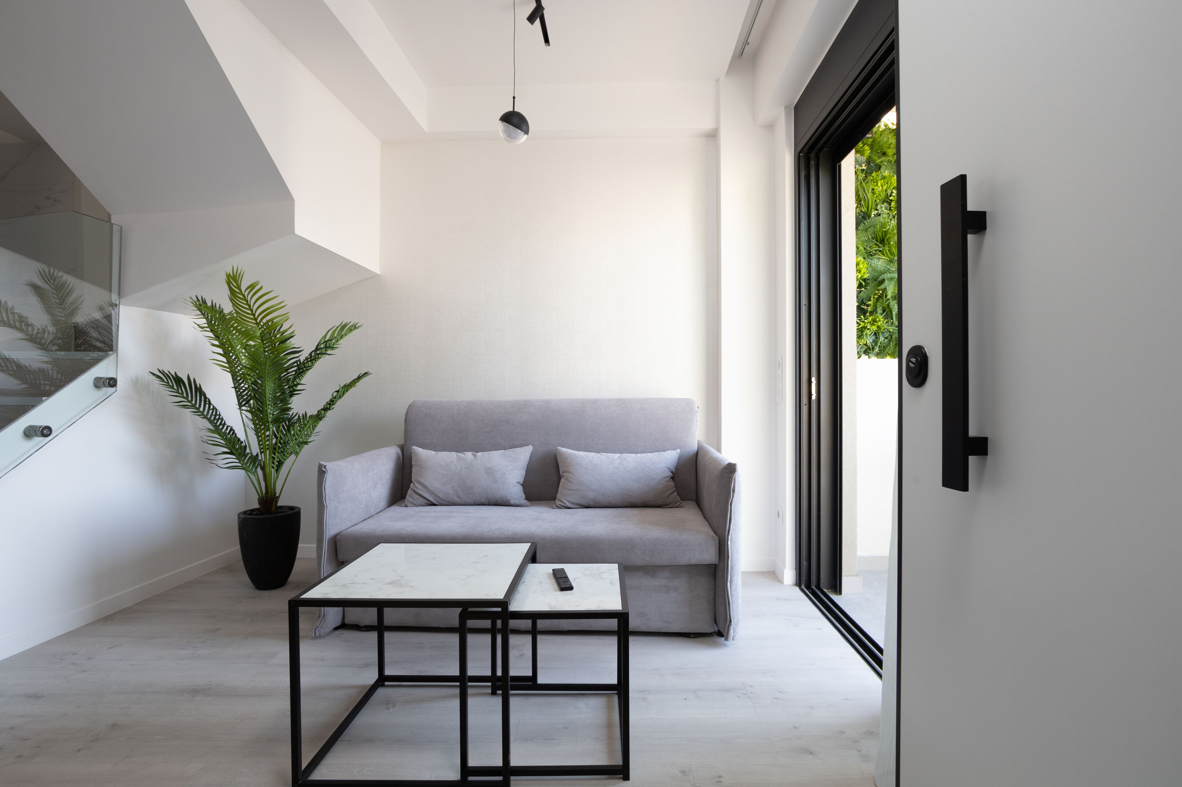 Una sala de estar moderna con un sofá gris, una mesa de centro, una planta en maceta y un ventanal grande.