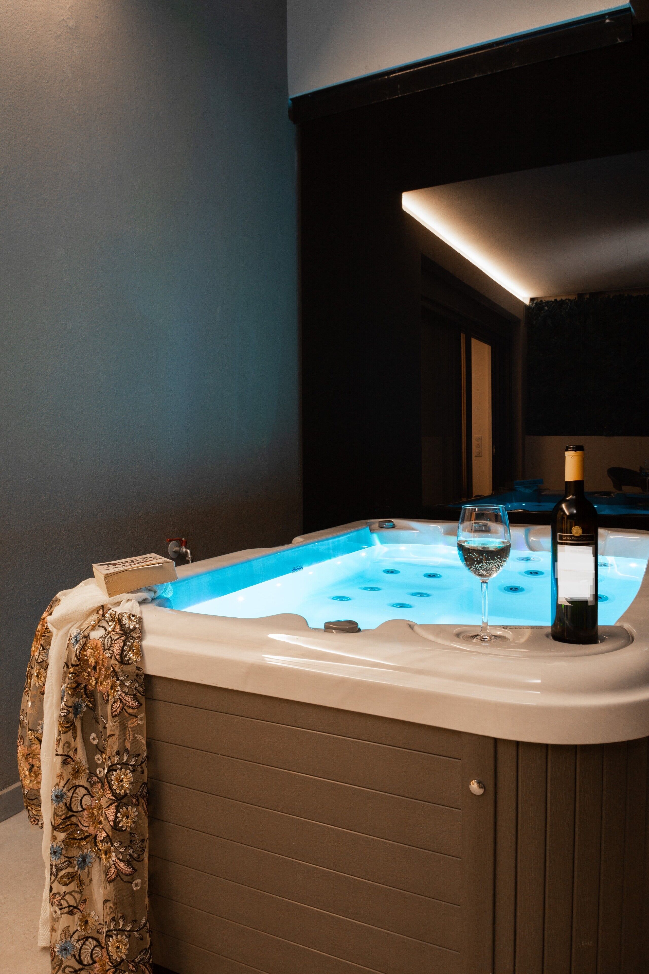 Ein Whirlpool mit einer Weinflasche und einem Glas, vor einer dunklen Wand mit einer Leuchte darüber.