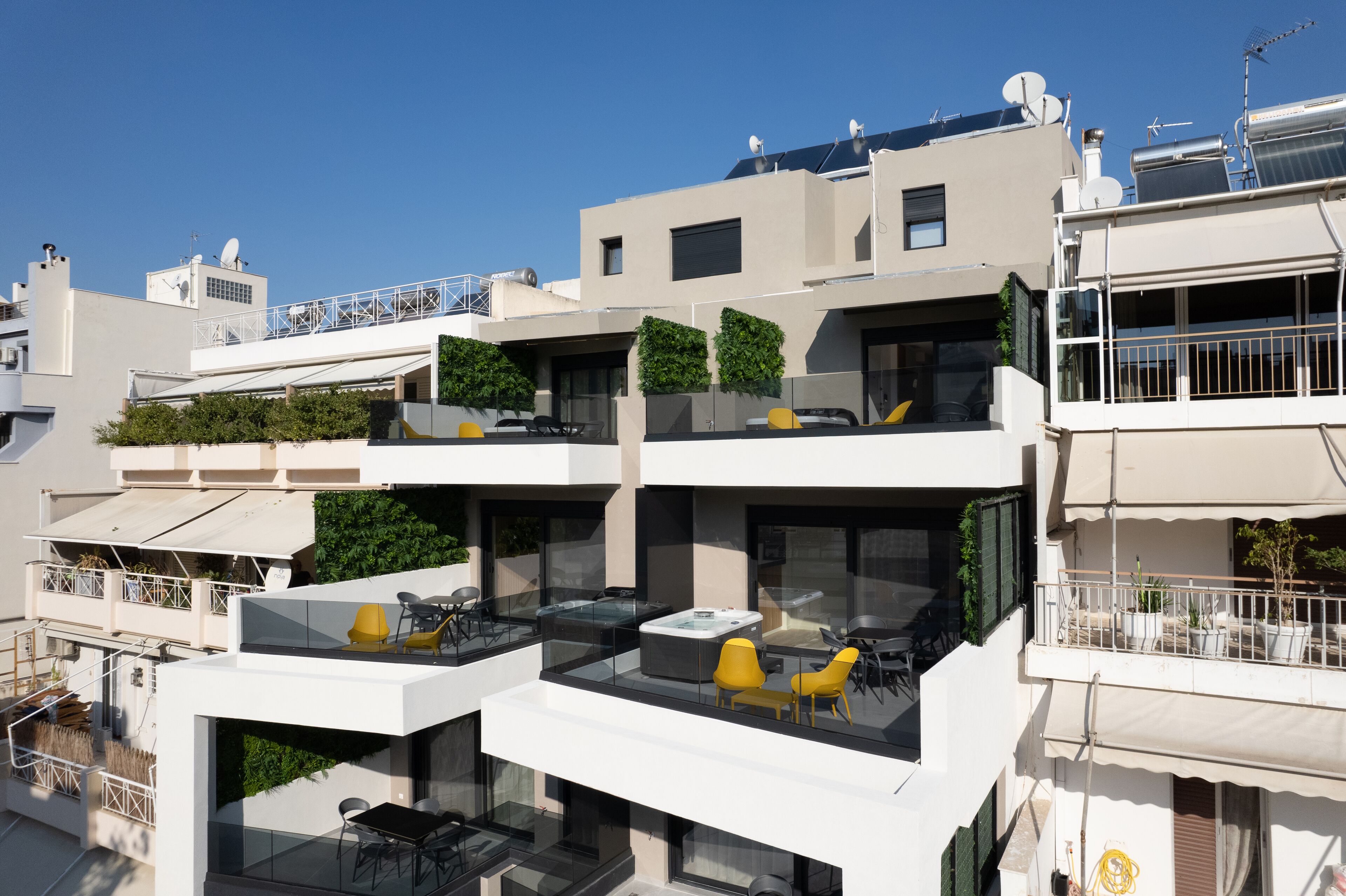 A modern multi-story building with balconies, outdoor seating, and solar panels.