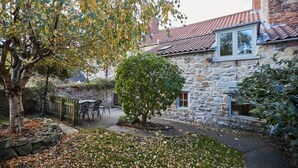 A stone building with a tiled roof, a small window, and a tree in the foreground. - Host & Stay | Hall Garth (Pickering)