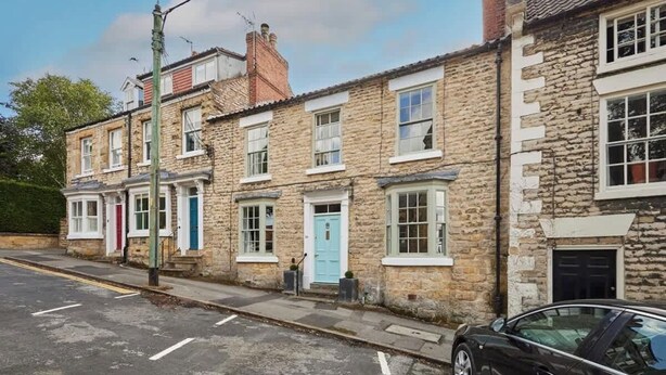 A row of stone houses with uniform windows and doors, a clear sky, and a parked car on the street. - Host & Stay | Hall Garth (Pickering)