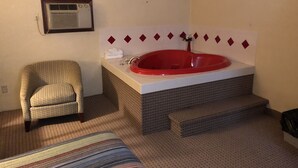 Camera d'albergo con vasca idromassaggio rossa, una poltrona e un letto a righe.