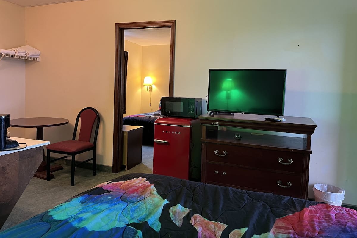 A hotel room with a bed, a desk with a computer, a chair, a television, and a microwave.