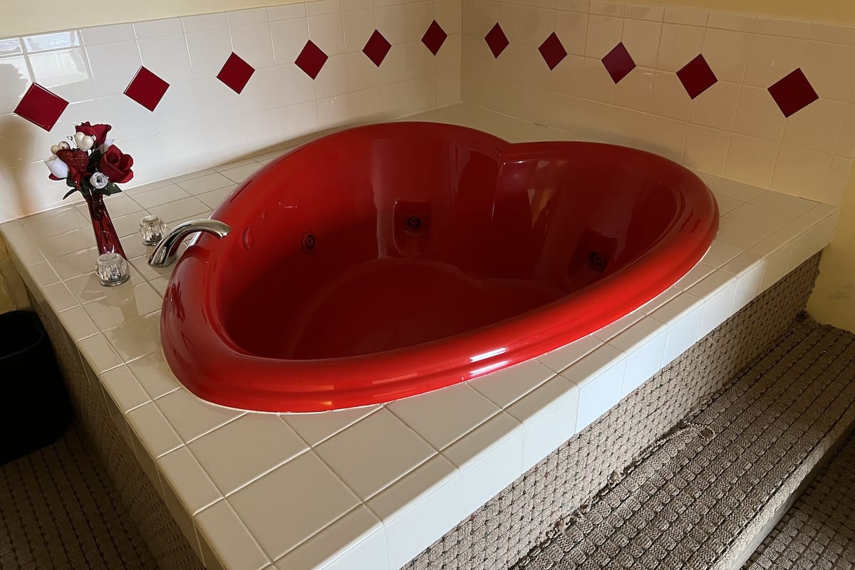 A red bathtub in a bathroom with white tiles and red diamond patterns on the wall.