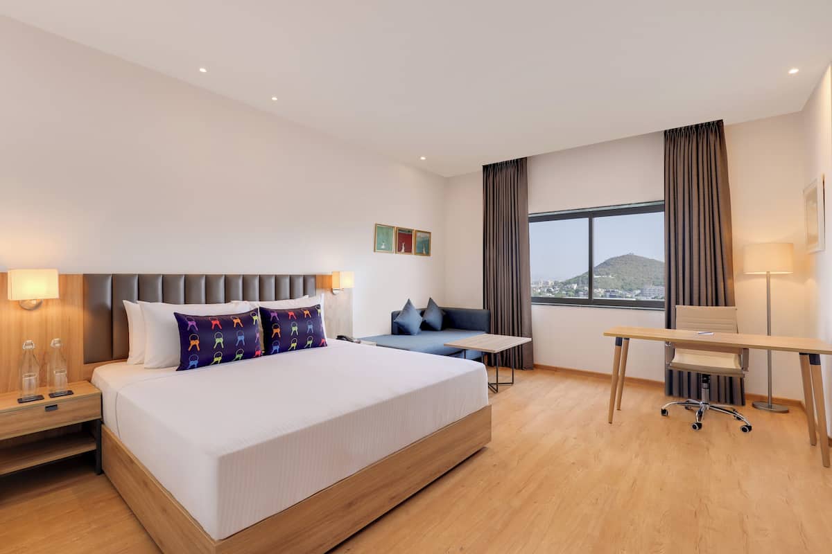 A modern hotel room with a large bed, a desk, and a view of a mountain.