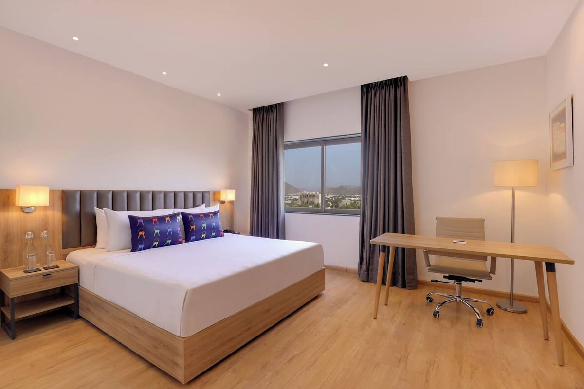 A hotel room with a large bed, a desk, and a view of the city.