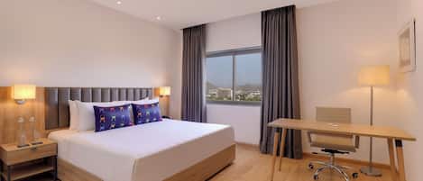 Un cuarto de hotel con una cama grande, un escritorio y vista a la ciudad.