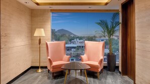 A modern room with two plush chairs, a small round table, a floor lamp, and a large window offering a city view.