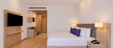 A modern hotel room with a large bed, bedside table, TV mounted on the wall, and a small desk area.