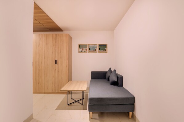 Una habitación minimalista con un sofá gris, una mesa de madera y un armario de madera.