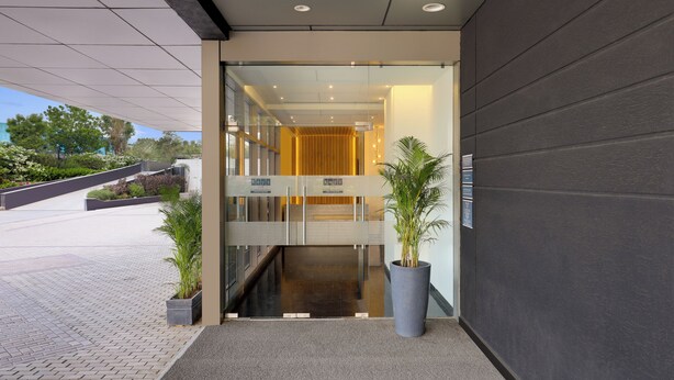 A modern hotel entrance with a glass door, a reception desk, and potted plants.