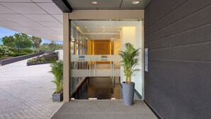 A modern hotel entrance with a glass door, a reception desk, and potted plants. - Keys Lite by Lemon Tree Hotels, Urban Square, Udaipur (Udaipur)